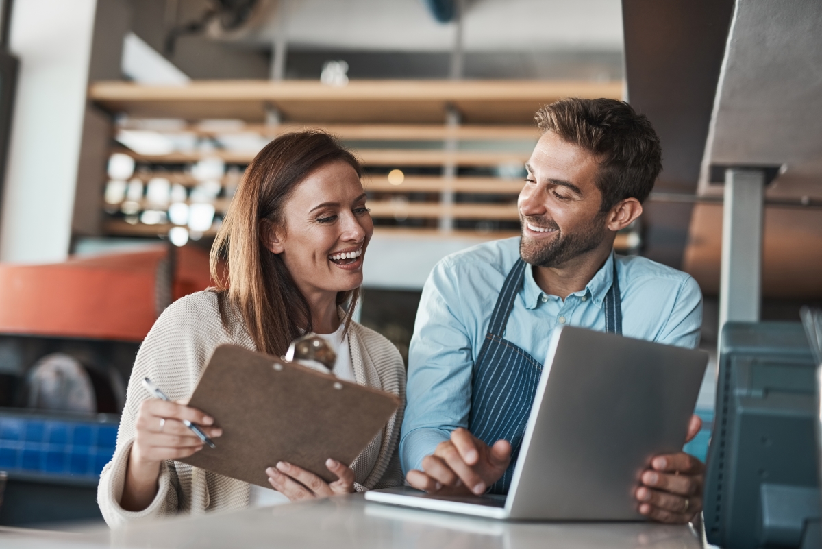 man and woman smiling while looking at a laptop screen